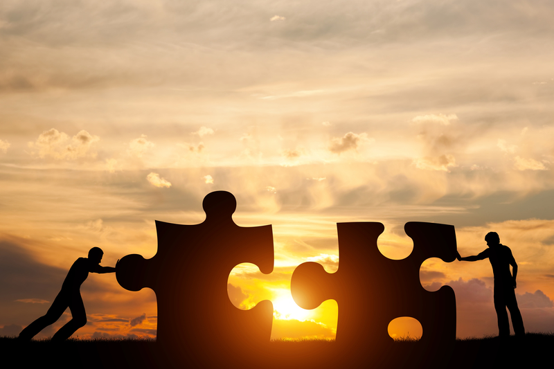 Two men connect two puzzle pieces. Sunset sky. Concept of business solution, teamwork, solving a problem, challenge